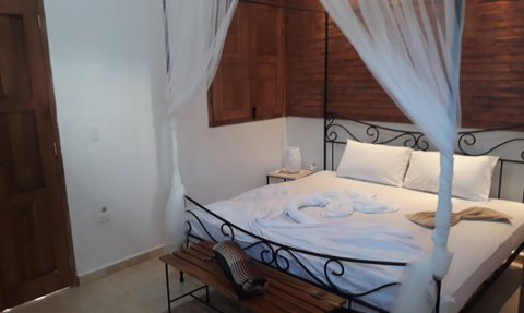 Ein gemütliches Schlafzimmer mit einem Himmelbett, weißen Laken und einem rustikalen Holzstuhl im Hintergrund.