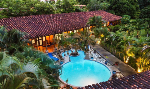 Ein Blick auf ein elegantes Anwesen mit einem glitzernden Pool, umgeben von üppigem Grün und sanft beleuchteten Palmen.