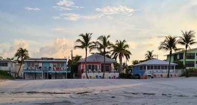 Bunte Strandhäuser stehen in einer Reihe, umgeben von Palmen und einem sanften, wolkigen Himmel über Fort Myers Beach.