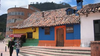 Bunte Fassade eines Cafés mit einem traditionellen Ziegeldach, umgeben von modernen Gebäuden und einer malerischen Landschaft.