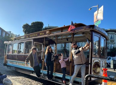 Eine Gruppe von vier Personen posiert fröhlich an einer historischen Kabelbahn in San Francisco, umgeben von sonnigem Wetter.