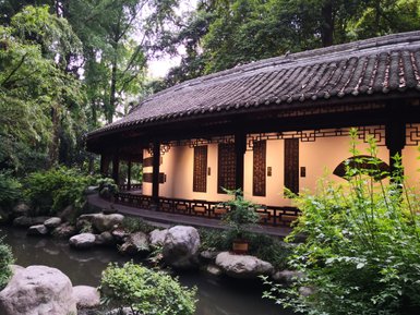 Ein traditionelles chinesisches Gebäude mit einem geschwungenen Dach, umgeben von üppigem Grün und einem ruhigen Teich.