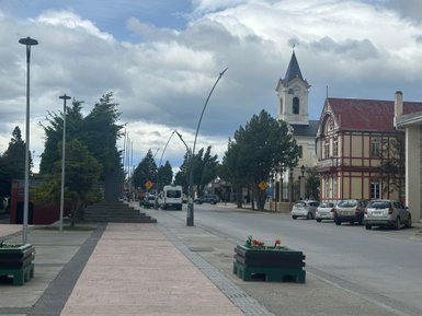 Eine ruhige Straße in Puerto Natales, gesäumt von Bäumen und historischen Gebäuden, unter einem bewölkten Himmel.