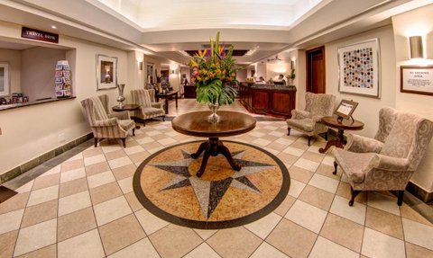 Der Empfangsbereich des Hotels zeigt elegante Stühle und einen runden Tisch mit einer großen Blumenvase in der Mitte.