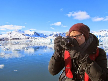 Eine Person mit einer Kamera steht am Wasser und fotografiert die beeindruckende Berglandschaft im Hintergrund.