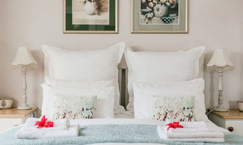 Ein gemütliches Schlafzimmer mit einem großen Bett, umgeben von weißen Kissen und dekorativen Kissen mit floralen Motiven.