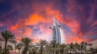Der Burj Al Arab erhebt sich majestätisch vor einem dramatischen Sonnenuntergang über Dubai, umgeben von Palmen.