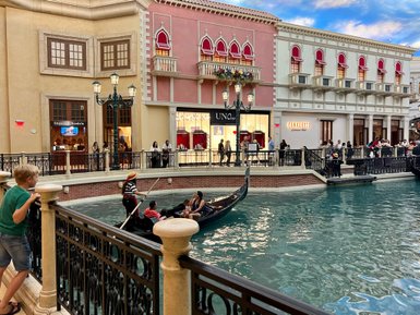 Ein Junge beobachtet fasziniert eine Gondelfahrt in einem nachgebauten venezianischen Ambiente mit Geschäften im Hintergrund.