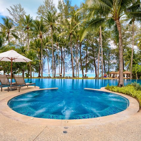 Ein einladender Pool umgeben von Palmen, mit Liegen und einem Sonnenschirm, der eine entspannte Urlaubsatmosphäre schafft.