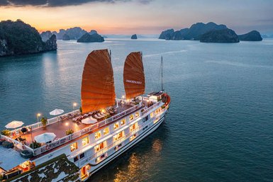 Ein traditionelles Schiff mit roten Segeln gleitet sanft über das ruhige Wasser der Halong-Bucht, umgeben von beeindruckenden Felsen.