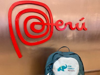 Ein grüner Rucksack mit einem Elefantenlogo steht vor einem roten Peru-Schild in einem modernen Innenraum.