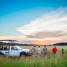 Eine Gruppe von fünf Personen steht in einem weiten Grasfeld, während die Sonne am Horizont untergeht.