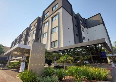 Das moderne Hotel Nadia Confort beeindruckt mit seiner stilvollen Architektur und einladender Pflanzenlandschaft im Vordergrund.