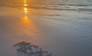 Am Strand sind im Sand die Worte 'HELLO' und ein Kreis zu sehen, während die Sonne am Horizont untergeht.