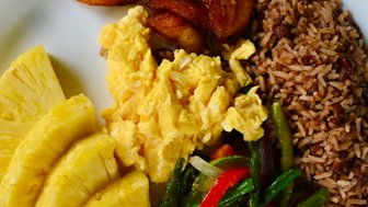 Eine appetitliche Mahlzeit mit gebratenen Bananen, Rührei, Reis und buntem Gemüse, serviert mit frischer Ananas.