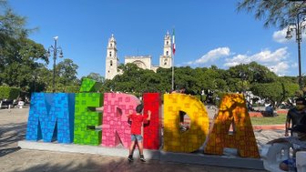 Kind posiert vor dem bunten Mérida-Schriftzug auf einem Platz in der Stadt – Mexiko Familienreise