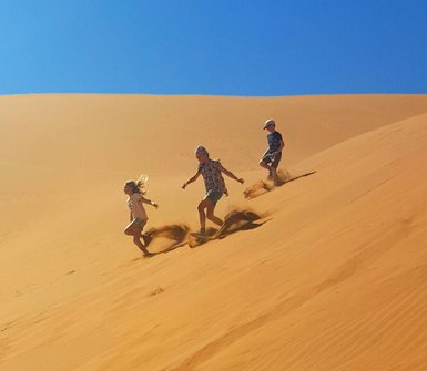 Drei Kinder laufen eine Düne hinunter - Namibia Rundreise mit Kindern