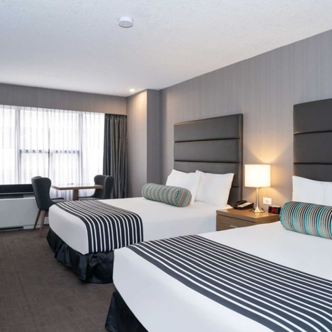 Ein modernes Hotelzimmer mit zwei Betten, eleganten Kopfenden und einem bunten Kissen in Calgary.