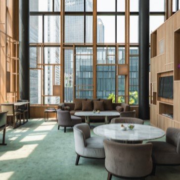 Ein eleganter Lobbybereich mit großen Fenstern, die viel Tageslicht hereinlassen, und modernen Möbeln aus Holz und Stoff.