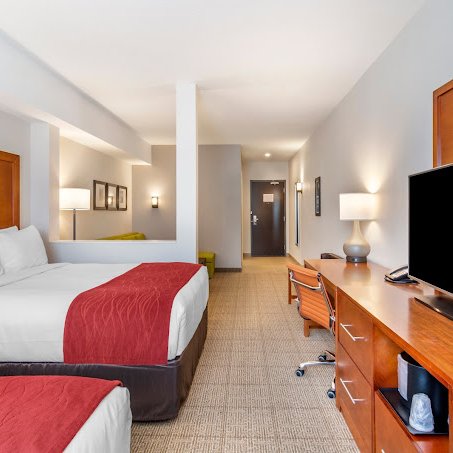 Ein modernes Hotelzimmer mit zwei Betten, einem großen Fernseher und einem Schreibtisch, das eine einladende Atmosphäre ausstrahlt.