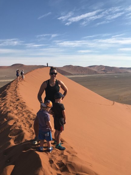 Eine Frau steht auf einer Sanddüne in Namibia, während zwei Kinder neugierig den Sand betrachten und die Landschaft genießen.