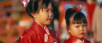 Zwei kleine Mädchen in traditioneller japanischer Kleidung, die mit Blumen im Haar an einem festlichen Ort stehen.