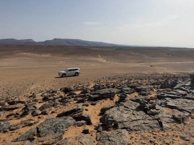 Ein silbernes SUV steht auf einer kargen Wüstenlandschaft, umgeben von steinigen Bögen und sanften Hügeln.