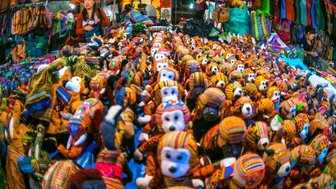 Ein lebhafter Nachtmarkt mit bunten, handgefertigten Stofftieren und einer Verkäuferin, die die Waren präsentiert.