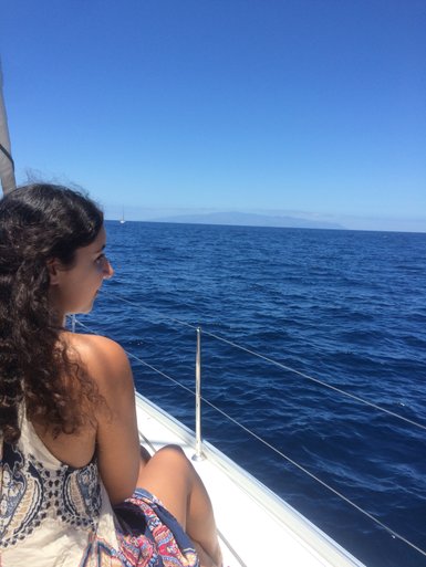 Eine Frau mit lockigem Haar sitzt entspannt auf einem Boot und blickt auf das weite, blaue Meer unter einem klaren Himmel.