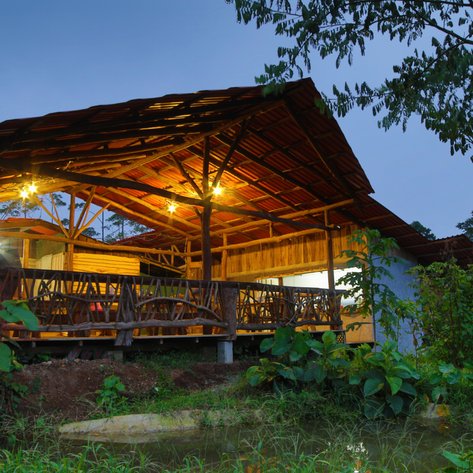 Ein rustikales Holzhaus mit einem großen, überdachten Balkon, umgeben von üppiger Vegetation und sanftem Licht in der Dämmerung.