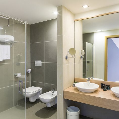 Ein modernes Badezimmer mit zwei Waschbecken, einem großen Spiegel und einer Dusche aus Glas, die hell erleuchtet ist.