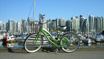 Ein grünes Fahrrad steht auf dem Gehweg, mit einer Marina und modernen Hochhäusern im Hintergrund.