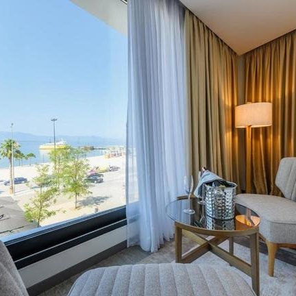 Ein elegantes Hotelzimmer mit Blick auf das Meer, umgeben von sanften Vorhängen und stilvollen Möbeln.