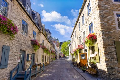 Eine malerische Gasse in Quebec, gesäumt von historischen Steinhäusern und blühenden Pflanzen in bunten Kästen.