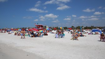 Ein belebter Strand mit vielen Menschen, bunten Sonnenschirmen und einem klaren blauen Himmel über Siesta Key.