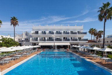 Ein einladender Poolbereich mit blauen Wasser und Sonnenschirmen, umgeben von Palmen und einem modernen Hotel im Hintergrund.