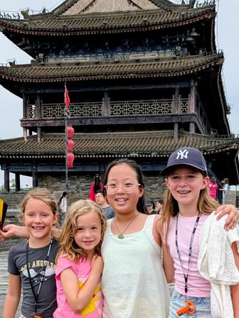 Vier Mädchen stehen fröhlich vor einem historischen Torturm in Xi'an und lächeln in die Kamera, während bunte Laternen im Hintergrund schweben.