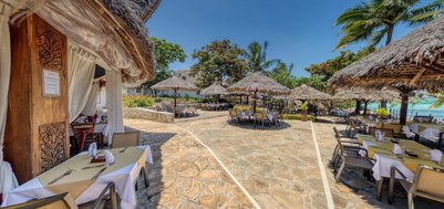 Ein einladendes Restaurant im Freien mit strohgedeckten Tischen und Blick auf das Meer, umgeben von Palmen und bunten Blumen.