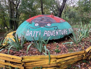 Eine bunte, kuppelförmige Struktur mit dem Schriftzug 'Dajti Adventure' steht in einem bewaldeten Bereich.