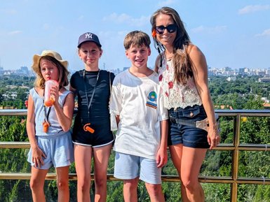 Vier Kinder und eine Frau stehen auf einem Aussichtspunkt, umgeben von Bäumen und City-Horizont, Freude strahlt aus ihren Gesichtern.