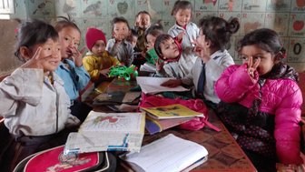 Eine Gruppe fröhlicher Kinder posiert in einem Klassenzimmer, einige zeigen das Peace-Zeichen mit ihren Händen.