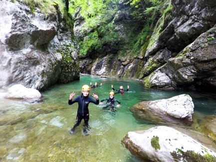 Eine Gruppe von Menschen in Neoprenanzügen genießt das Wasser eines klaren Flusses, umgeben von hohen Felsen und Bäumen.