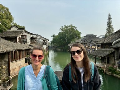 Zwei Frauen stehen auf einer Brücke über einen ruhigen Kanal, umgeben von traditionellen chinesischen Gebäuden.