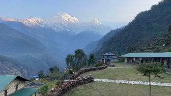 Ein atemberaubender Blick auf die schneebedeckten Annapurna-Berge, umgeben von grünen Tälern und traditionellen Häusern.