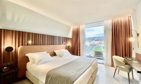 Ein modernes Hotelzimmer mit zwei Betten, eleganter Holzverkleidung und großen Fenstern, die einen Blick auf die Berge bieten.