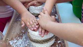 Mehrere Hände von Kindern drücken gemeinsam auf runde Käseformen, während sie in einer fröhlichen Umgebung arbeiten.