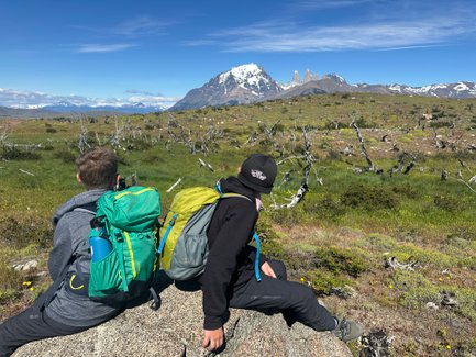 Zwei Kinder sitzen auf einem Felsen und blicken auf die beeindruckenden Torres del Paine in der Ferne.