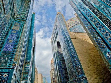 Blick auf die kunstvoll verzierten Wände des Shah-i-Zinda Komplexes in Samarkand, umgeben von strahlend blauem Himmel.