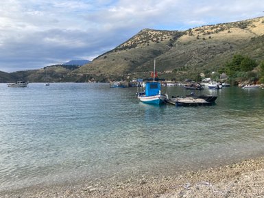 Ein ruhiger Hafen mit mehreren Booten, umgeben von sanften Hügeln und klarem Wasser, das die Landschaft widerspiegelt.