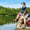 Zwei Jugendliche sitzen auf einem Felsen am Wasser, während einer mit einem Fernglas in die Ferne schaut.